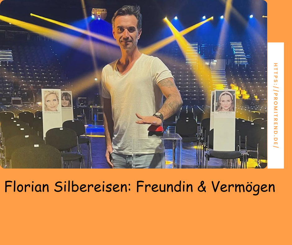 Ein Mann in einem weißen T-Shirt steht in einer leeren Veranstaltungshalle mit Scheinwerfern im Hintergrund. Der Text "Florian Silbereisen: Freundin & Vermögen" ist unten auf dem Bild zu sehen.