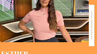 Eine Frau in einem rosa Oberteil steht in einem Fernsehstudio mit einem Fußballspiel im Hintergrund. Der Name "Esther Sedlaczek" ist unten im Bild zu sehen.