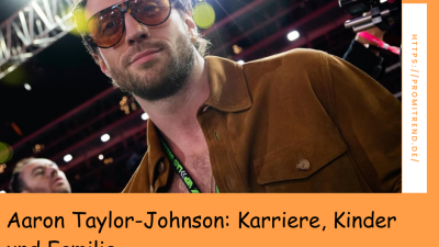 Person mit brauner Jacke und Lanyard steht vor einer hell erleuchteten Bühne. Text: "Aaron Taylor-Johnson: Karriere, Kinder und Familie".