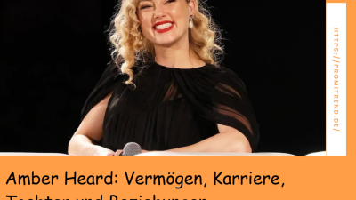 Eine Person mit lockigem blondem Haar sitzt auf einer Bühne und hält ein Mikrofon. Der Text auf dem Bild lautet: "Amber Heard: Vermögen, Karriere, Tochter und Beziehungen".