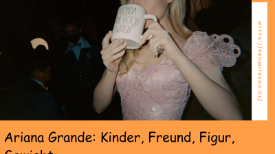 Eine Person in einem rosa Kleid hält eine Tasse mit der Aufschrift "GOOD WITCH". Im Hintergrund sind weitere Personen zu sehen.