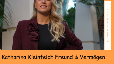 Eine Frau mit verdecktem Gesicht trägt einen weinroten Blazer mit Blumenapplikationen und steht vor einer tropischen Kulisse. Der Text auf dem Bild lautet "Katharina Kleinfeldt Freund & Vermögen".